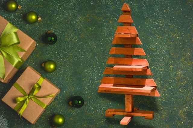 Arbre de Noël en bois traité couleur bois exotique, décoration écologique et originale pour les fêtes, posé à côté de cadeaux et boules vertes