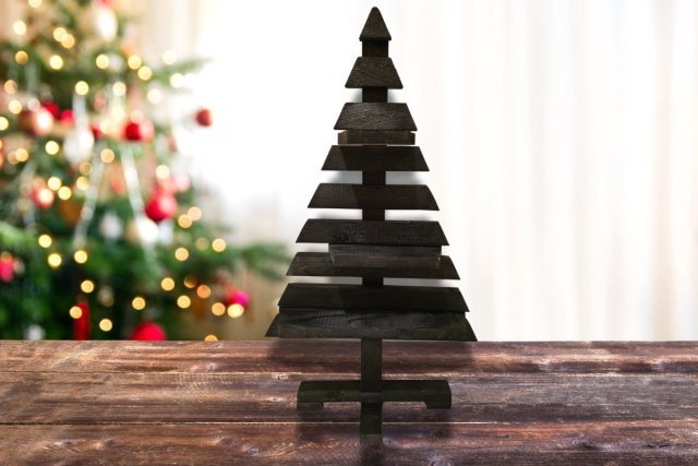 Sapin-bois-noir en bois naturel issu de palettes, décoration originale et écologique pour Noël, posé sur une table en bois devant un sapin lumineux
